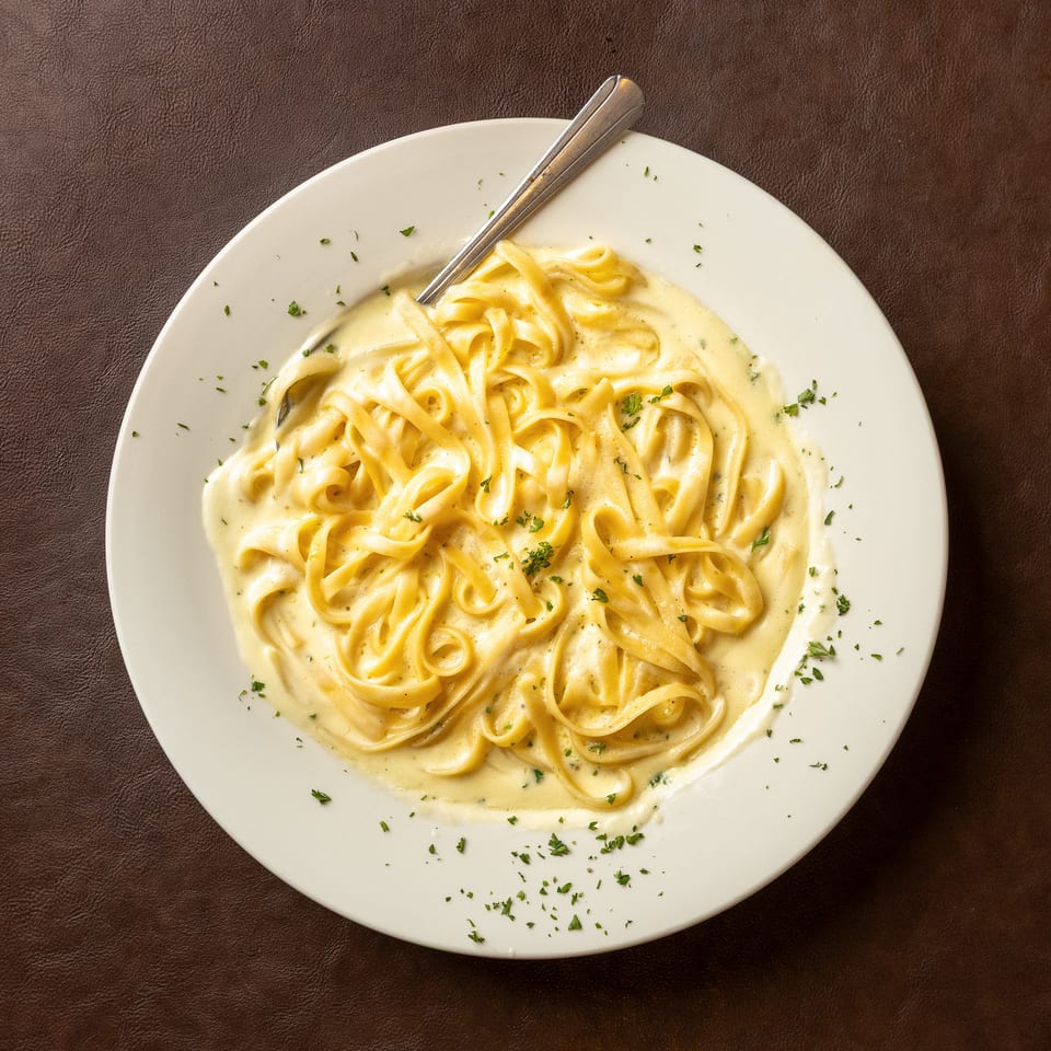Creamy fettuccine Alfredo garnished with parsley on a white plate, with a fork resting on top.