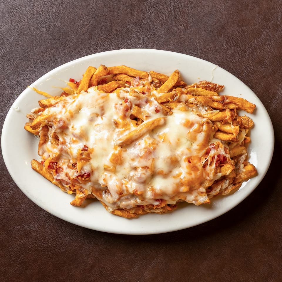 Crispy fries topped with melted cheese and bacon bits on a white oval plate against a dark brown background.
