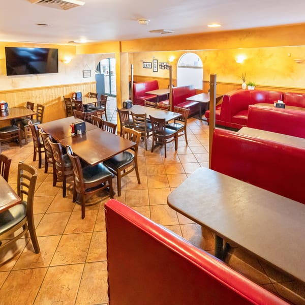 Warmly lit restaurant dining room with wooden tables, chairs, red leather booths, tiled floors, and wall-mounted televisions.