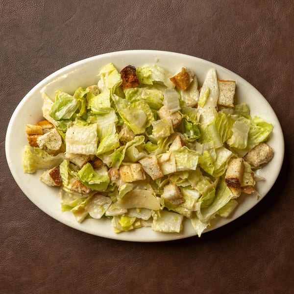 Caesar salad with crisp romaine lettuce, creamy dressing, croutons, and grilled chicken served on a white oval plate.