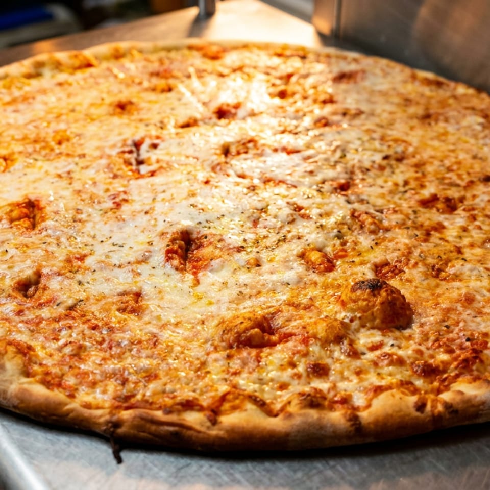 A large, freshly baked cheese pizza with a golden crust sits on a stainless steel counter.