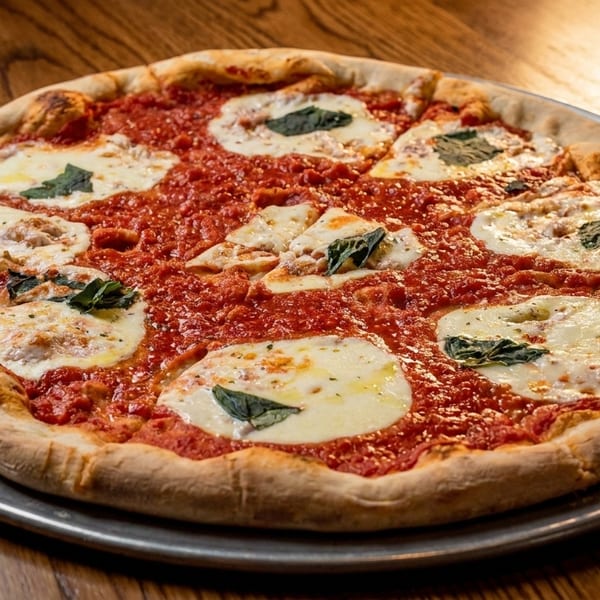 A whole Margherita pizza with fresh mozzarella, tomato sauce, and basil on a metal pan.