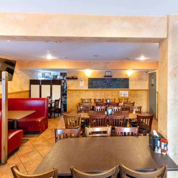 Warmly lit restaurant dining room with red booths, wooden tables and chairs, tiled floors, and a chalkboard menu.